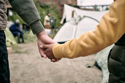 Rear view of unrecognizable children of different ages holding hands while coming in to migrant camp