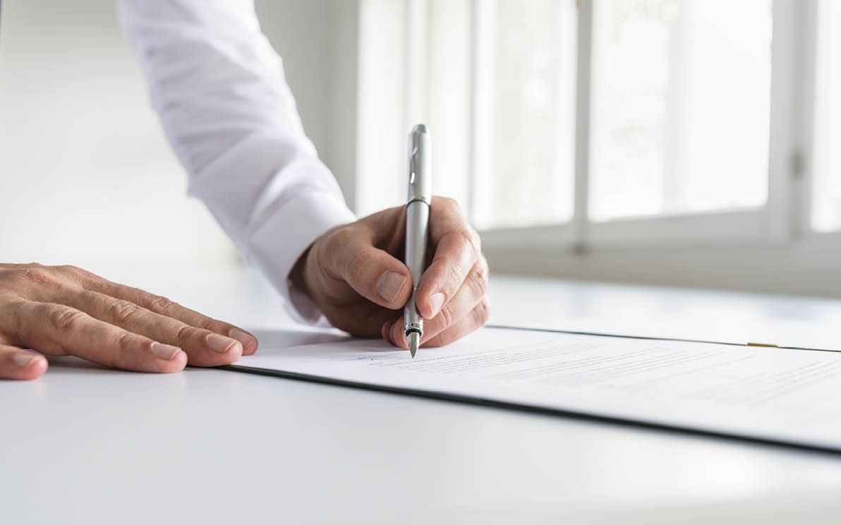 Businessman in white shirt signing contract, document or legal papers in a bright office.